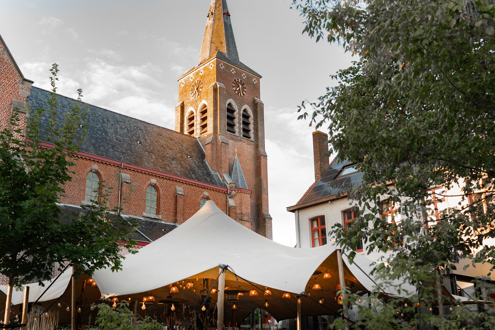 Outdoor dining terrace with historic church steeple backdrop, white canopy, string lights and basket lamps